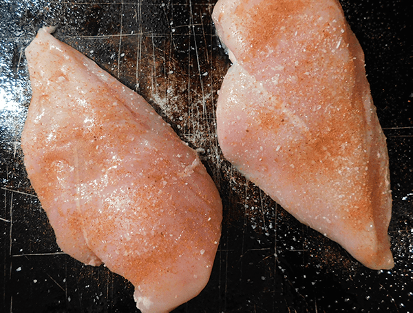 Two raw chicken breasts on a baking sheet