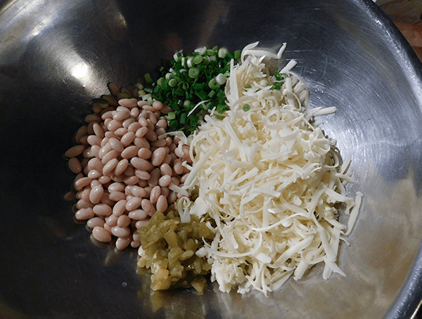 Shredded cheese, green onions, white beans and chiles in a silver bowl