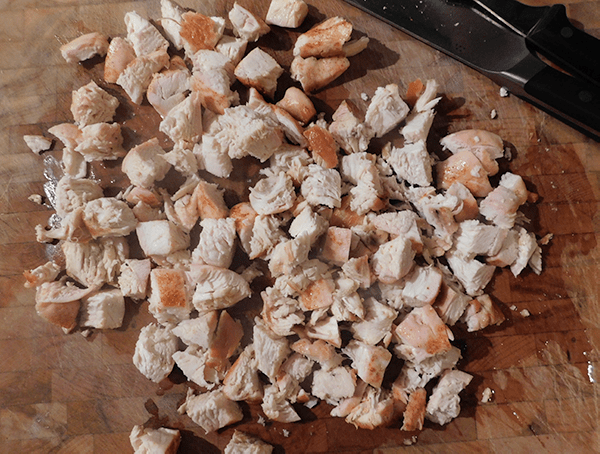 Baked chicken cut into pieces on a chopping block with knife in upper corner