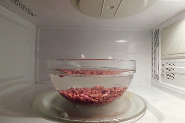 Dried red beans covered with water by 2" in a clear bowl in a microwave