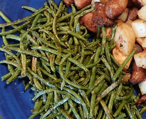 Roasted green beans on a blue platter next to fried potatoes