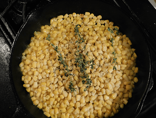 frozen corn kernels in a cast iron skillet with thyme branches on top