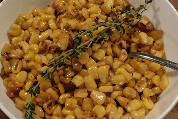 Charred ccooked corn with thyme in a white bowl with a silver spoon