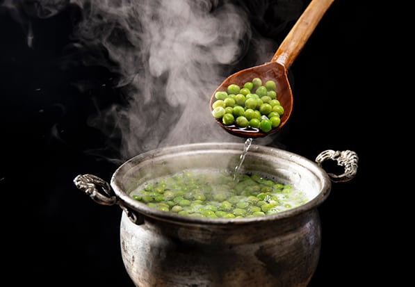 Peas in a pot of boiling water with a wooden spoon