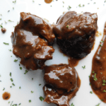 Cubes of beef in brown gravy on white plate