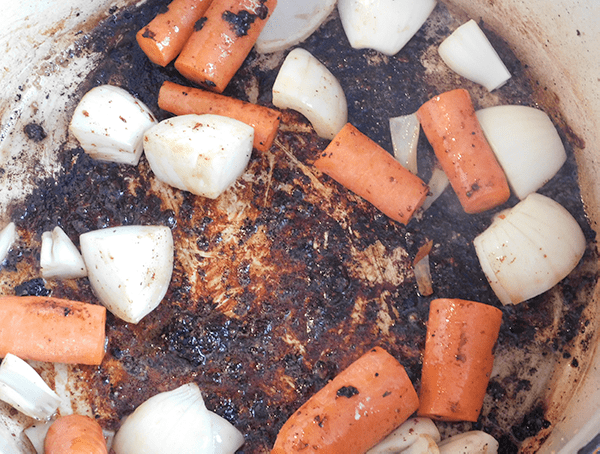 Carrots and onions in bottom of dutch oven covered in fond from searing beef