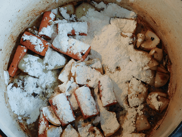 Flour sprinkled over carrots and onion in dutch oven