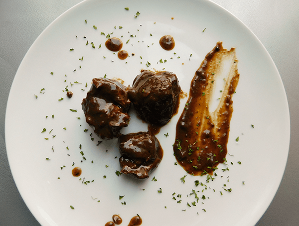 Beef cubes in brown gravy on a white plate sprinkled with parsely