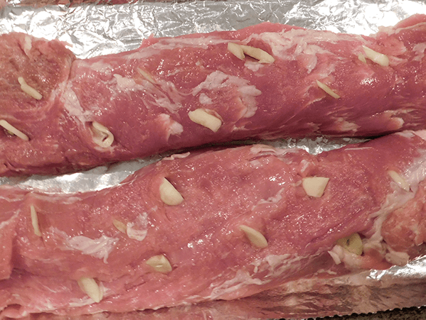 Close up picture of pork tenderloin with sliced garlic studding it
