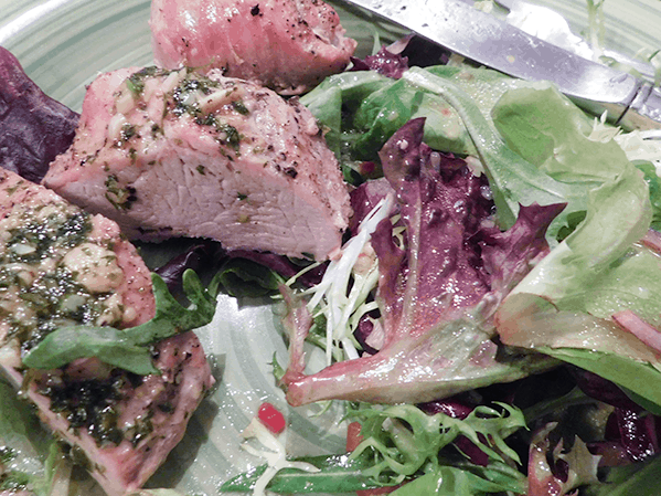 Close up of pork tenderloin on a plate with side salad