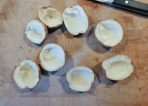 Baked potatoes on a chopping block with insides scooped out