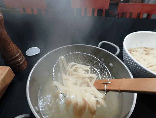 Cooked Noodles being removed from a pan of hot water with an asian strainer
