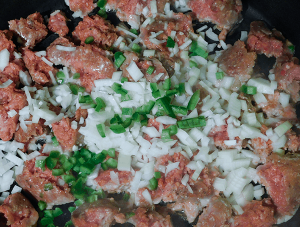 Sausage, chopped onions and jalapenos cooking in a cast iron skillet