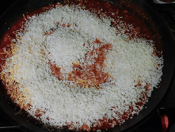 Cast iron skillet with tomato mixture under dry quick-cook rice.