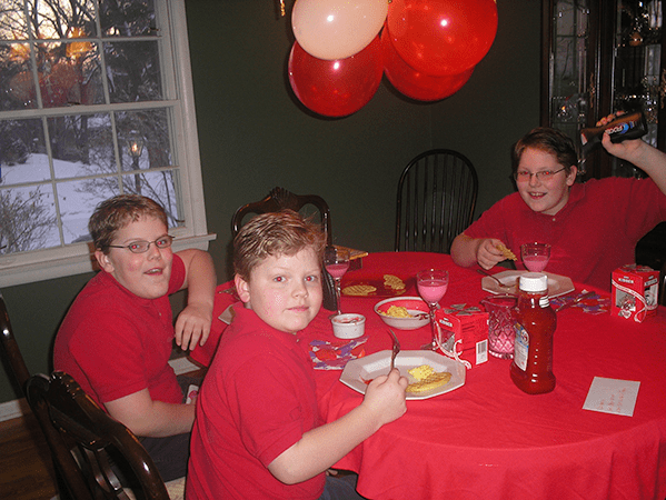 Picture of three boys around a dining room table in red uniforms