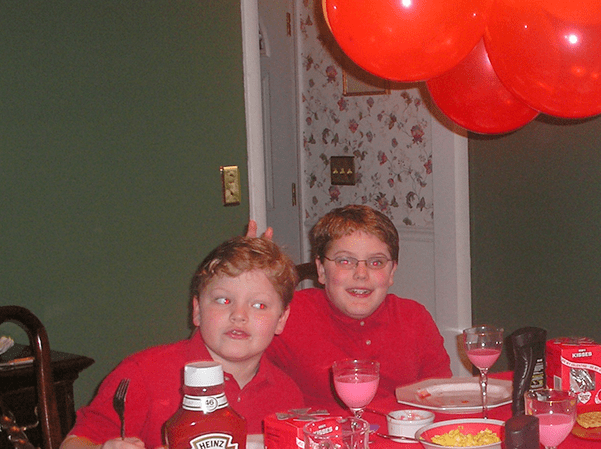 Two boys at breakfast in dining room in red uniforms, one holding up bunny ears behind another