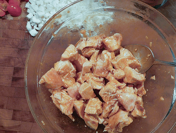 Sauced baked chicken pieces in a clear bowl with a silver spoon on a chopping block ready for Buffalo Chicken Nachos