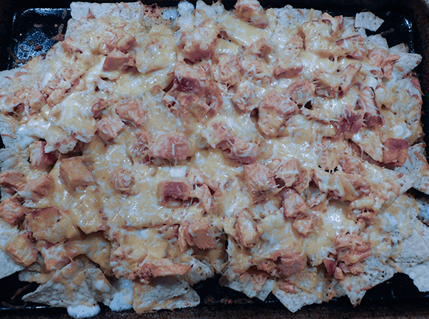 Melted cheese on top of Buffalo Chicken Nachos on a sheet pan