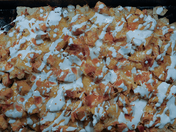 Cooked Buffalo Chicken Nachos getting a drizzle of ranch dressing