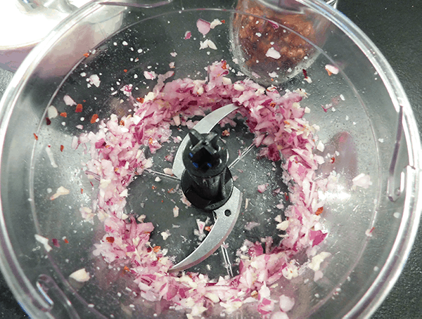 Chopped red onion and garlic in food processor prepping Chimichurri Sauce