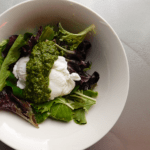 Baby Greens with poached egg coated with chimichurri sauce in a white bowl