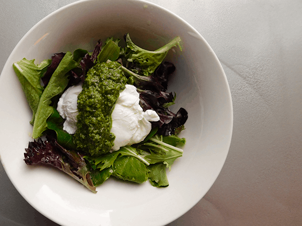 Baby Greens with poached egg coated with chimichurri sauce in a white bowl