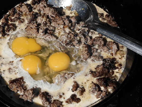 Cooked ground beef in cast iron skillet with eggs start a low carb cheeseburger pie