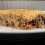 Side view of cooked cheeseburger pie on a white plate with green beans