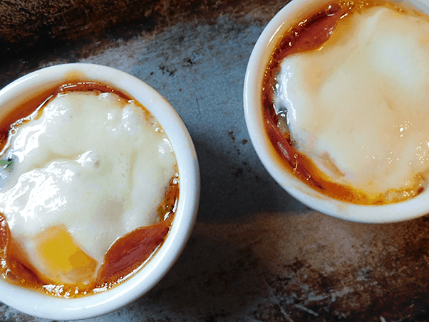 Two ramekins full of Baked Eggs on baking sheet