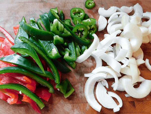 Sliced Red, green and jalapeno peppers on a chopping block with yellow onions