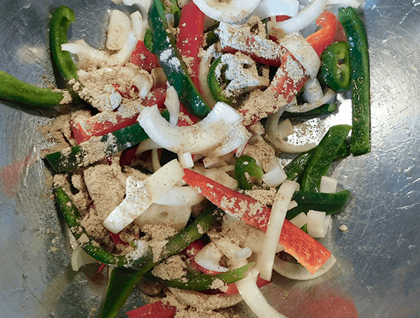 Peppers and onions in a big bowl with fajita seasoning sprinkled on top