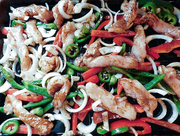 Seasoned sliced veggies and chicken on a sheet pan ready to cook