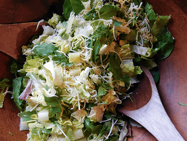 Mixed lettuces with shredded cheese in a wooden salald bowl