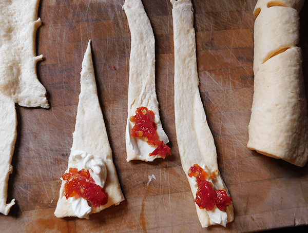 Crescent rolls cut in thirds, with cream cheese on wide end, with a dollop of red pepper jelly