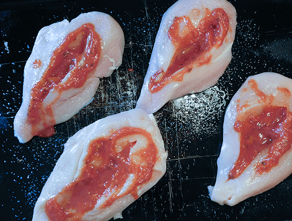 Chicken cut open with marinara sauce spread inside, ready for stuffing