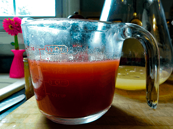 Strawberry jelly melted into water in a glass measuring cup