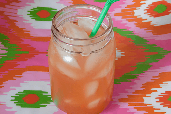 Strawberry Lemonade in small mason jar with a green bendy straw on a multicolored background