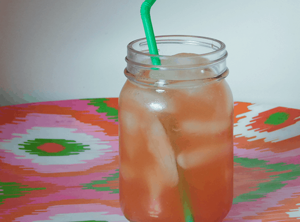Strawberry Lemonade in a small mason jar with a green bendy straw on a multicolored platter