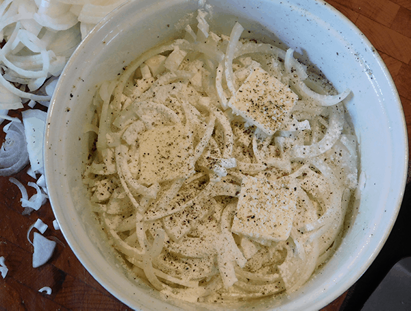 Sliced onions in a round white casserole dish sprinkled with flour, salt & pepper.