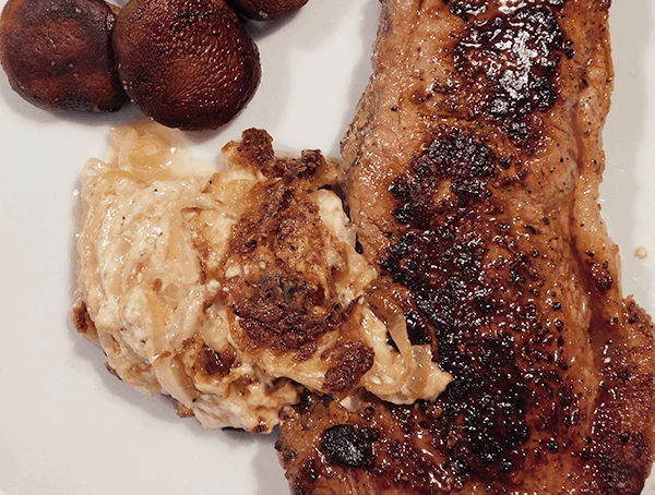 Scalloped Onions next to a cooked strip steak and mushrooms on a white plate