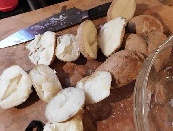 Baked potatoes are halved on a chopping block