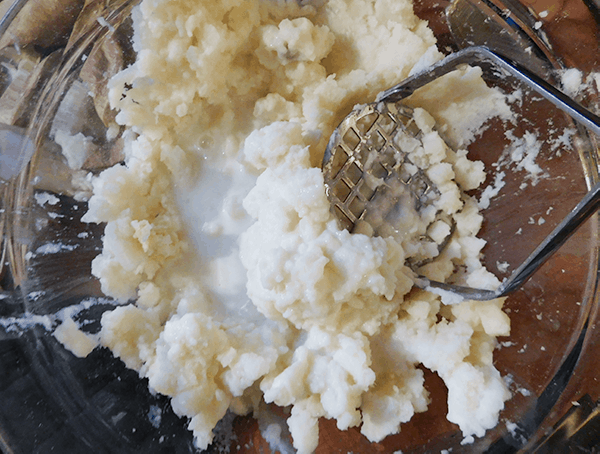 Potato innards and buttermilk in a glass bowl with a potato masher