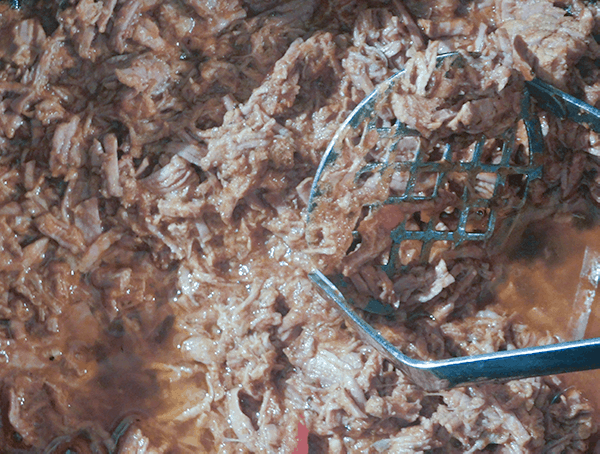 Shredded Italian Beef Sandwiches filling with a potato masher