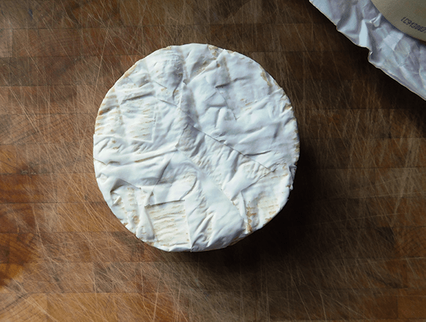 Brie on chopping block for Maple Walnut Baked Brie