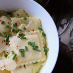 Ravioli in Broth in white bowl with parmesan cheese in background