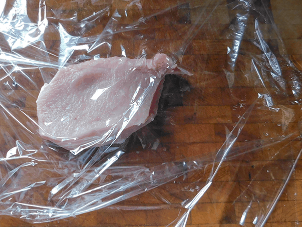 Trimmed raw pork chops om plastic wrap