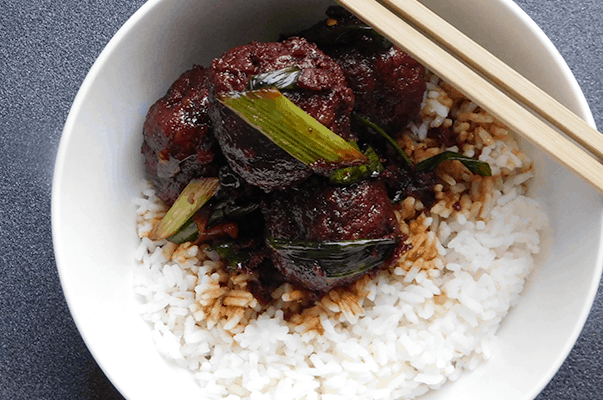 Mongolian Meatballs in a white bowl on white rice with chopsticks