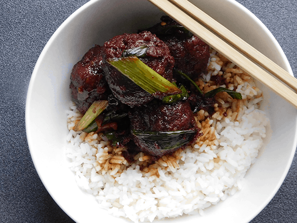 Mongolian Meatballs in a white bowl on white rice with chopsticks
