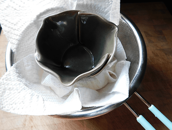 Small bowl on top of ricotta wrapped in paper towels in strainer