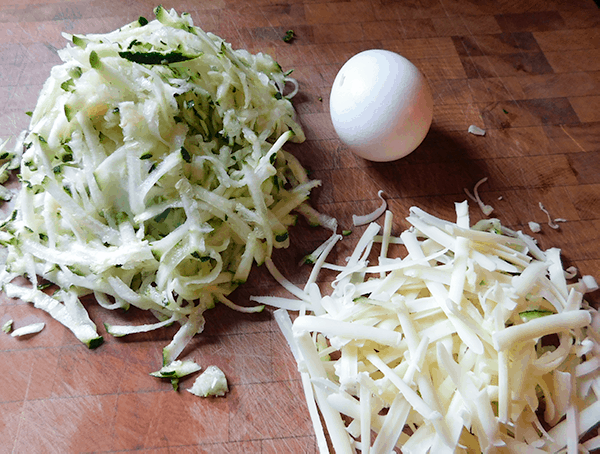 Grated zucchini, cheese and an egg on a cutting board